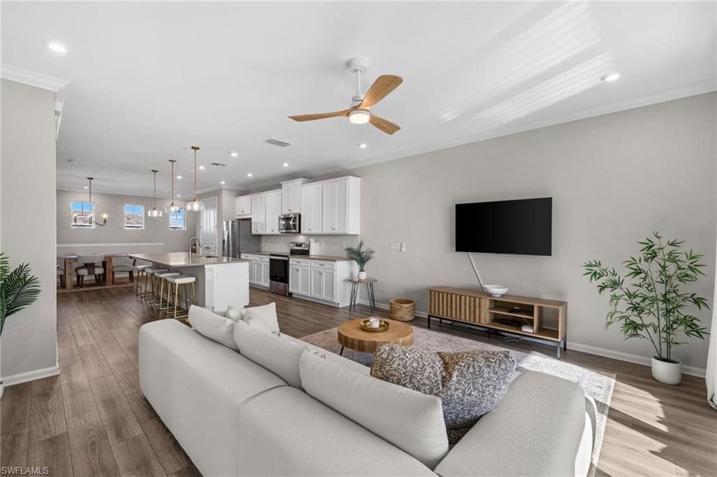 Living room with ornamental molding, a ceiling fan, dark wood-type flooring, recessed lighting, and a chandelier