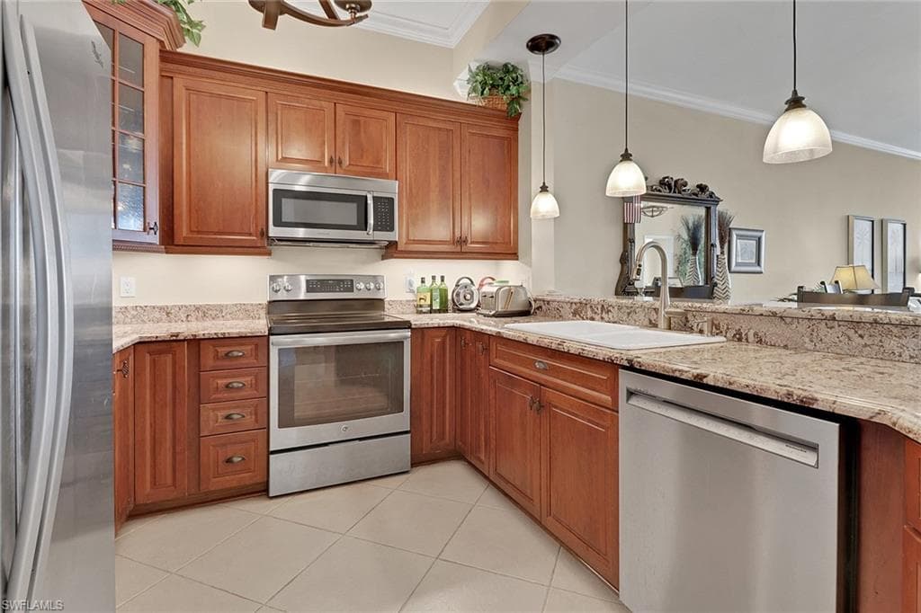 Kitchen featuring brown cabinetry, appliances with stainless steel finishes, pendant lighting, crown molding, and light tile patterned flooring