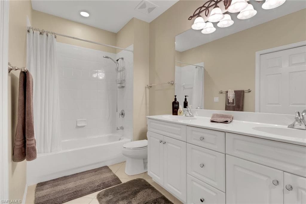 Full bathroom with light tile patterned floors, shower / bath combination with curtain, double vanity, and a chandelier