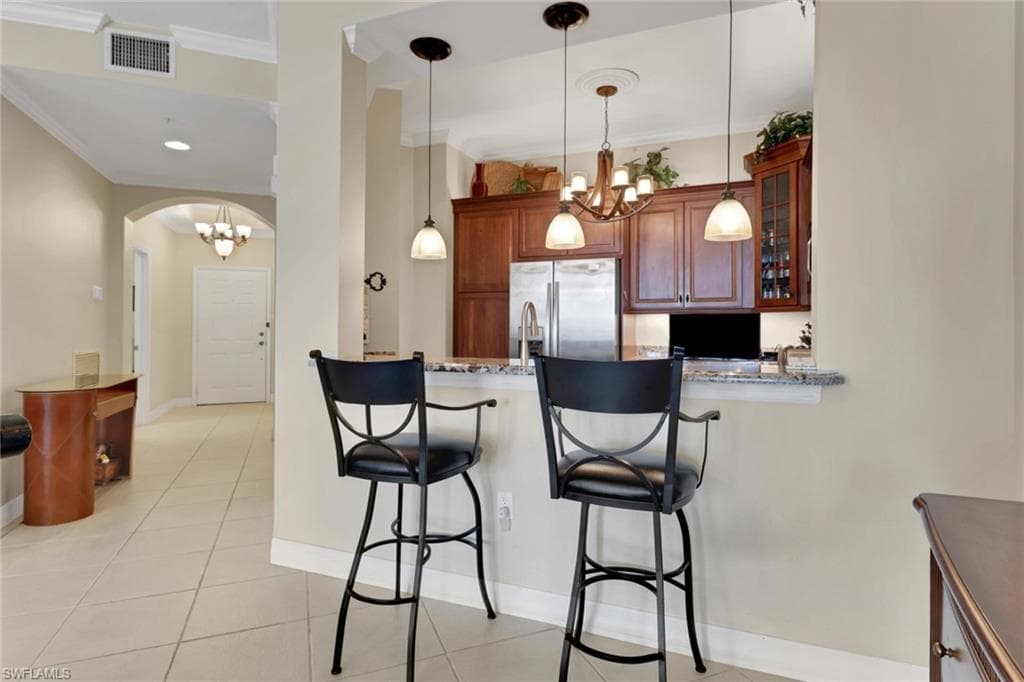 Kitchen featuring a kitchen bar, a chandelier, stainless steel refrigerator with ice dispenser, decorative light fixtures, and light tile patterned floors