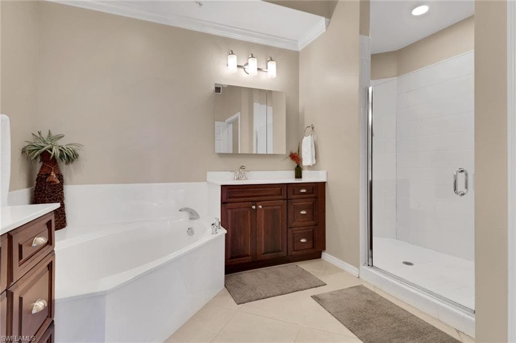 Full bathroom with light tile patterned floors, vanity, a garden tub, a shower stall, and crown molding