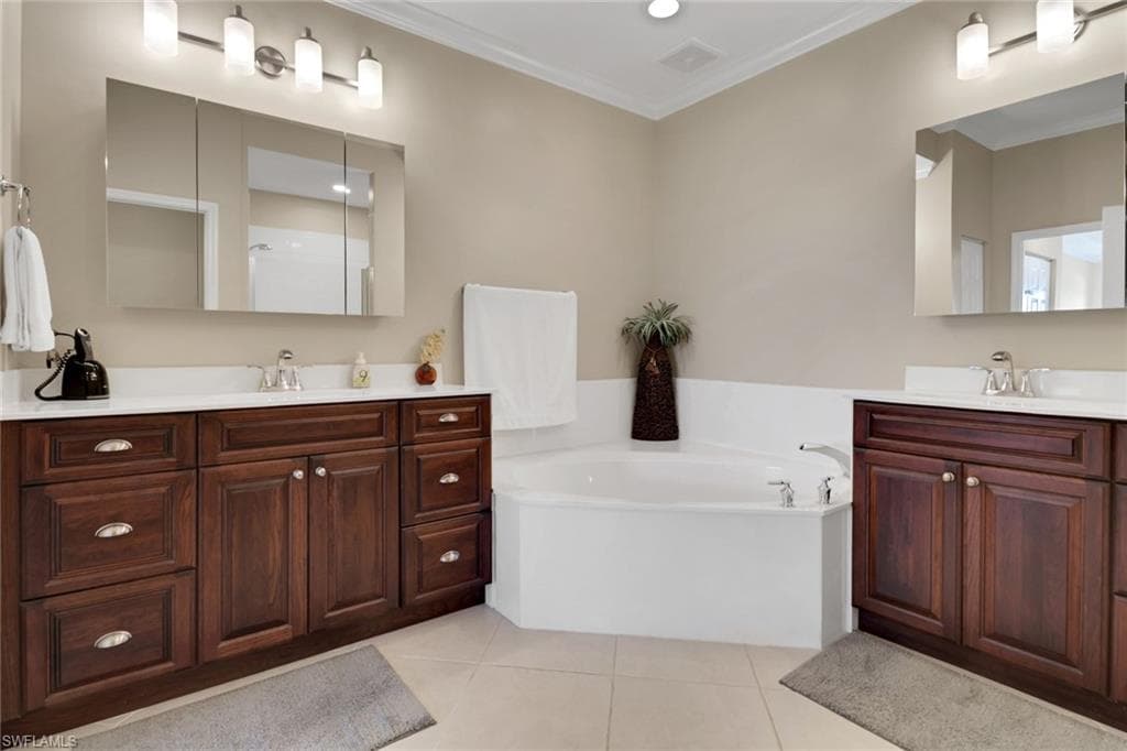 Full bath with light tile patterned floors, ornamental molding, two vanities, a garden tub, and a stall shower