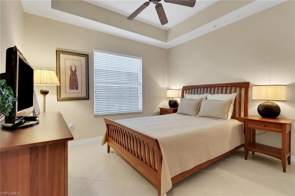 Bedroom featuring light tile patterned floors, a tray ceiling, and ceiling fan