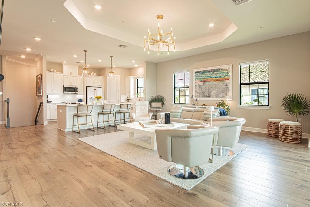 Living room featuring light wood finished floors, a raised ceiling, a chandelier, and recessed lighting