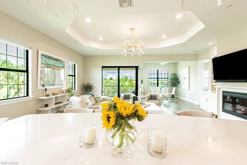 Living room with a glass covered fireplace, wood finished floors, a chandelier, recessed lighting, and a tray ceiling
