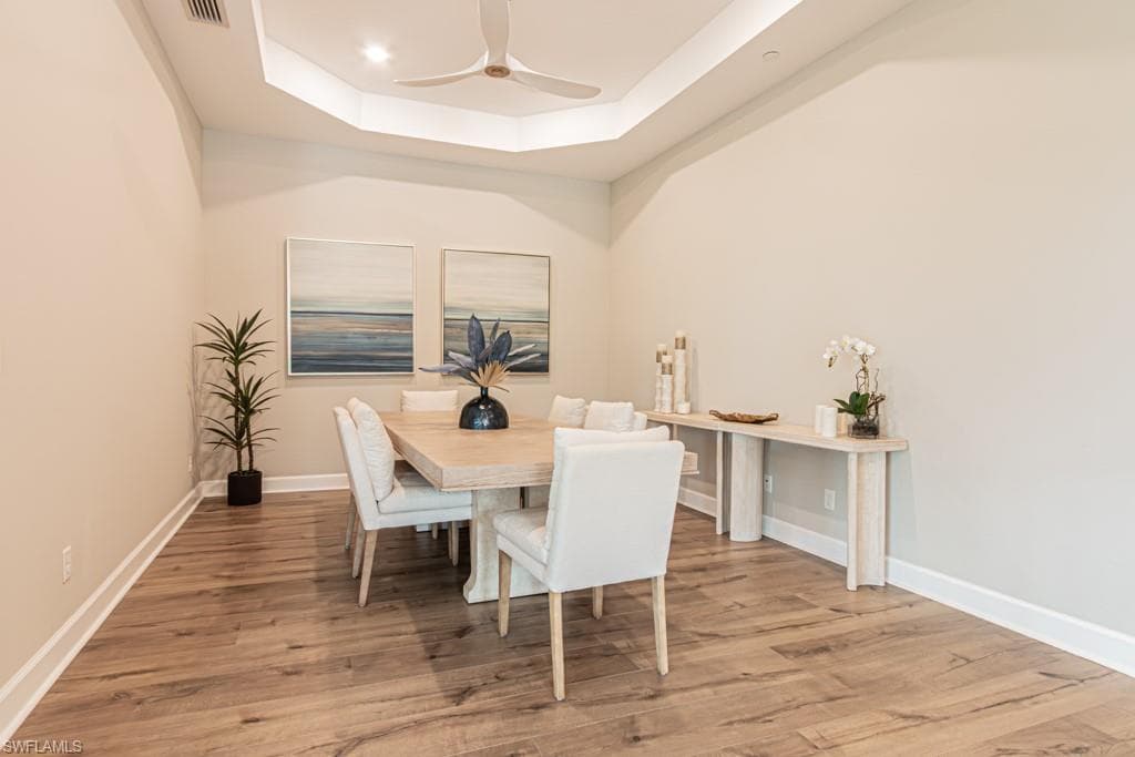 Dining area featuring a raised ceiling, light wood finished floors, and ceiling fan