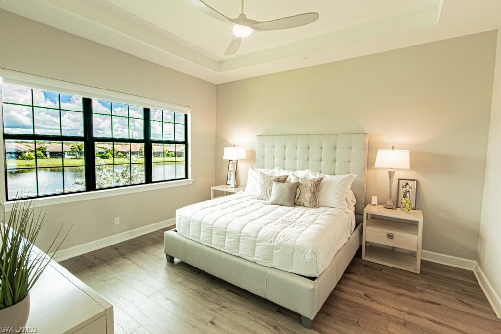 Bedroom featuring a raised ceiling, wood finished floors, a ceiling fan, and a water view