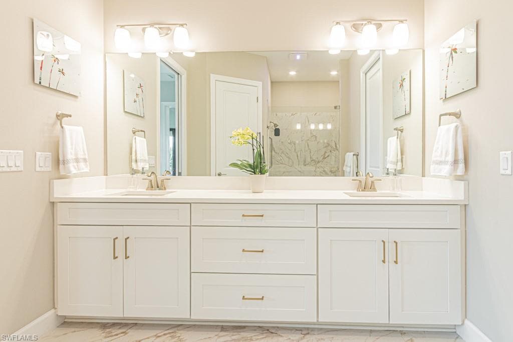 Full bathroom with double vanity, light marble finish floors, and a marble finish shower
