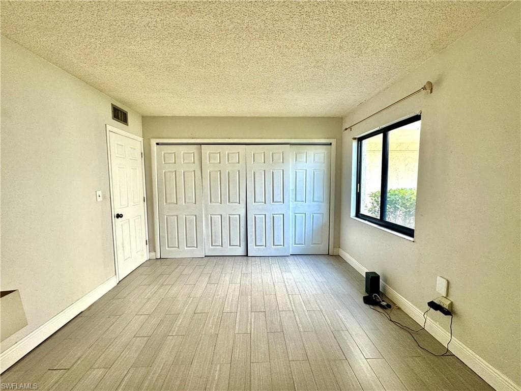 Unfurnished bedroom with a textured ceiling, light wood-style floors, and a closet