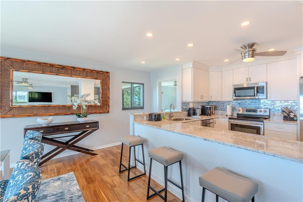 Kitchen with a ceiling fan, a breakfast bar area, appliances with stainless steel finishes, light stone counters, and white cabinets - Virtually Edited Image