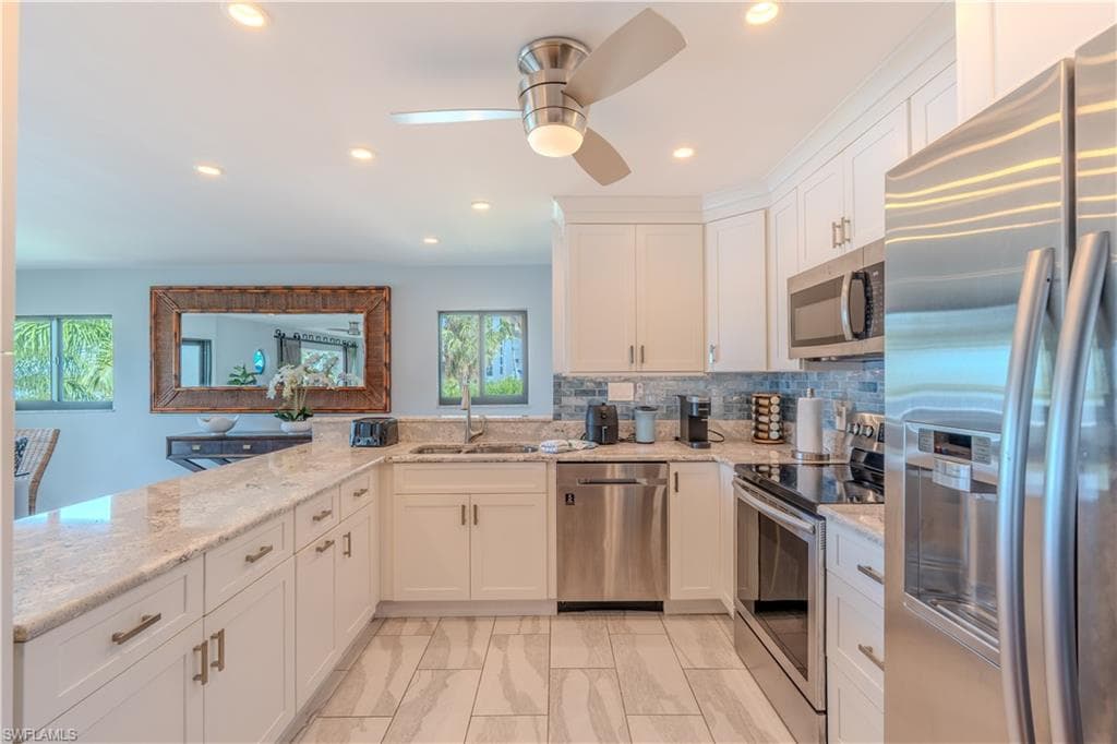 Kitchen with stainless steel appliances, light stone counters, white cabinetry, decorative backsplash, and recessed lighting - Virtually Edited Image