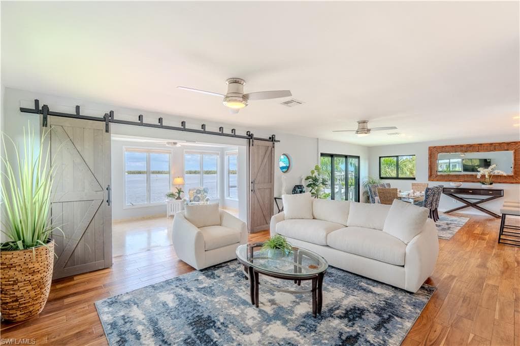 Living room with a barn door, a ceiling fan, and light wood flooring - Virtually Edited Image
