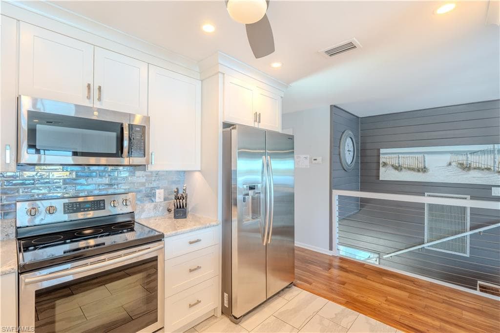 Kitchen with stainless steel appliances, white cabinets, recessed lighting, light stone counters, and backsplash - Virtually Edited Image