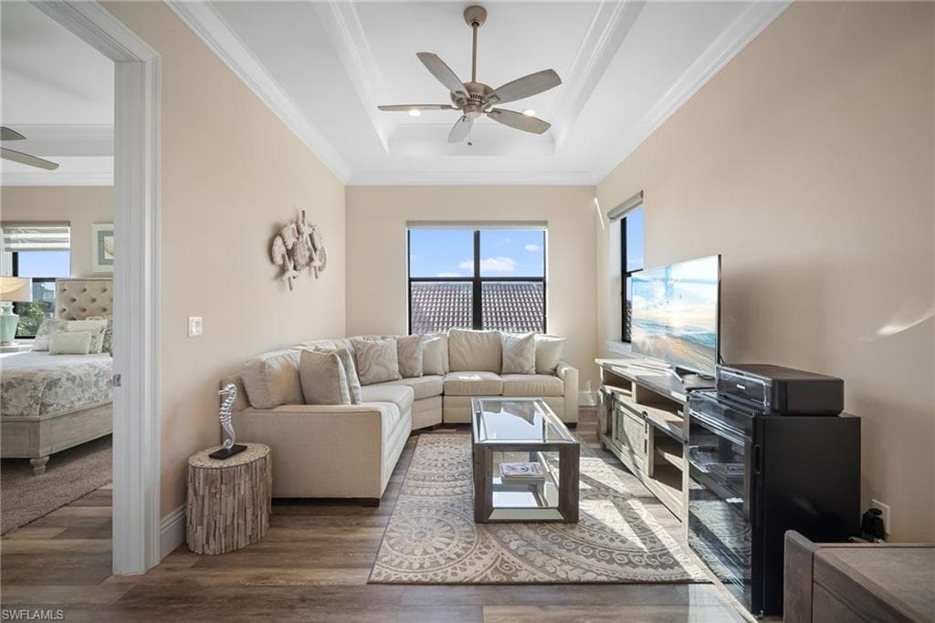 Den featuring ornamental molding, a tray ceiling, wood finished floors, and a ceiling fan