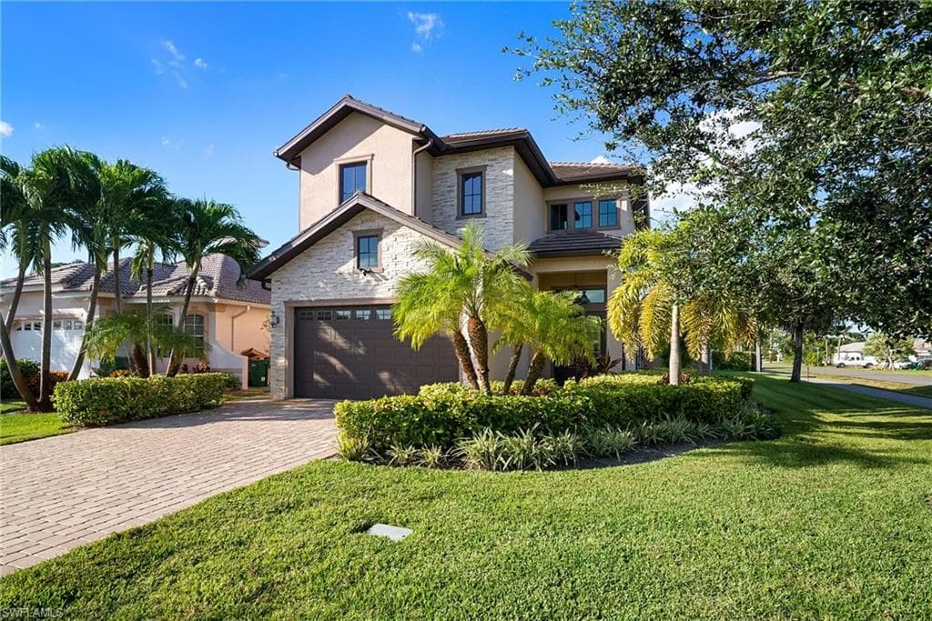 View of front of home featuring stone siding, stucco siding, decorative driveway, and a front lawn