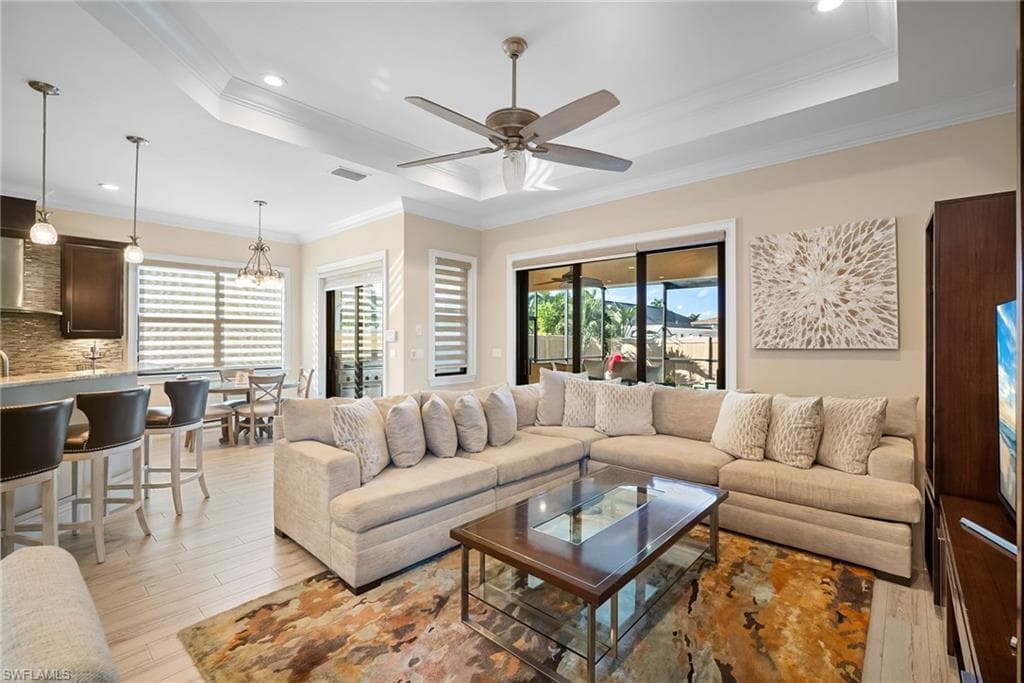 Living room with light wood-style flooring, crown molding, a tray ceiling, recessed lighting, and a chandelier
