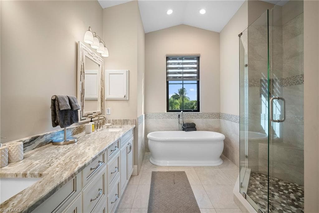 Bathroom featuring a freestanding tub, a stall shower, tile walls, double vanity, and light tile patterned floors