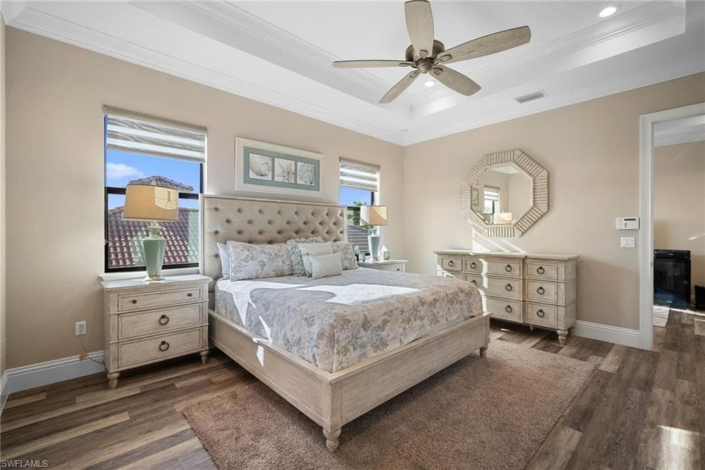 Bedroom with a tray ceiling, dark wood-style flooring, recessed lighting, crown molding, and a ceiling fan