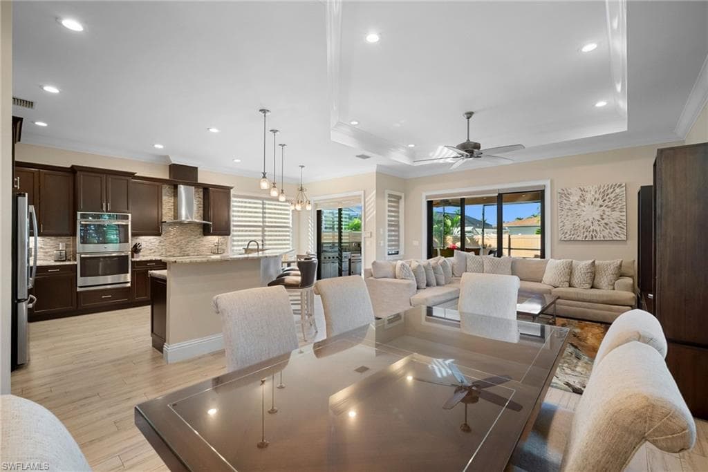 Dining area with a chandelier, ornamental molding, a tray ceiling, recessed lighting, and a ceiling fan
