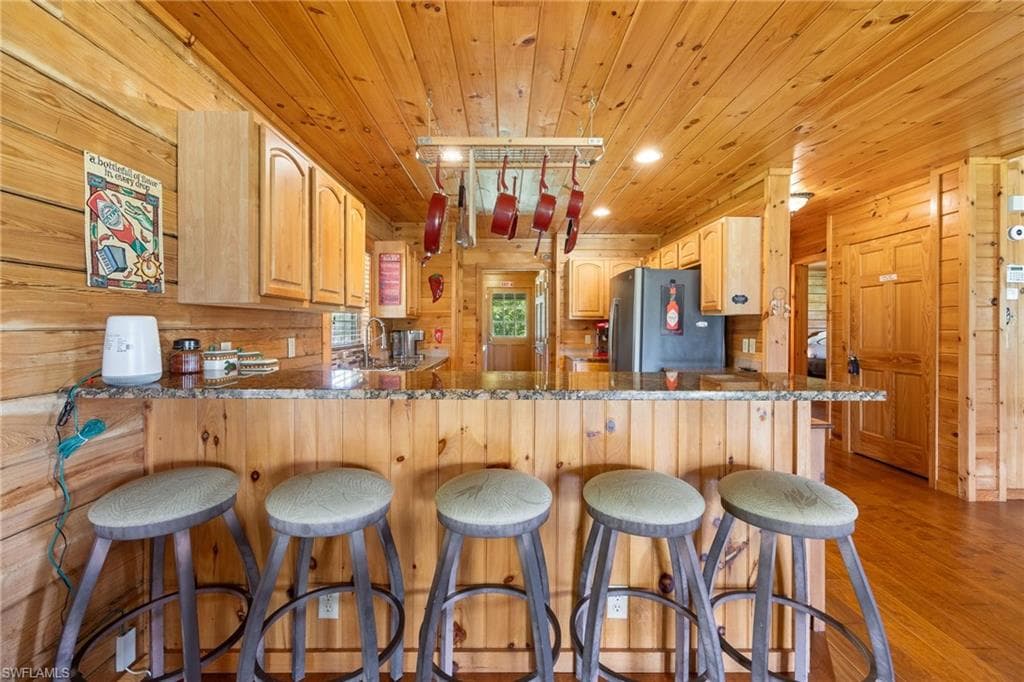 Kitchen with wooden walls, light wood finish cabinetry, light wood-style flooring, a peninsula, and freestanding refrigerator