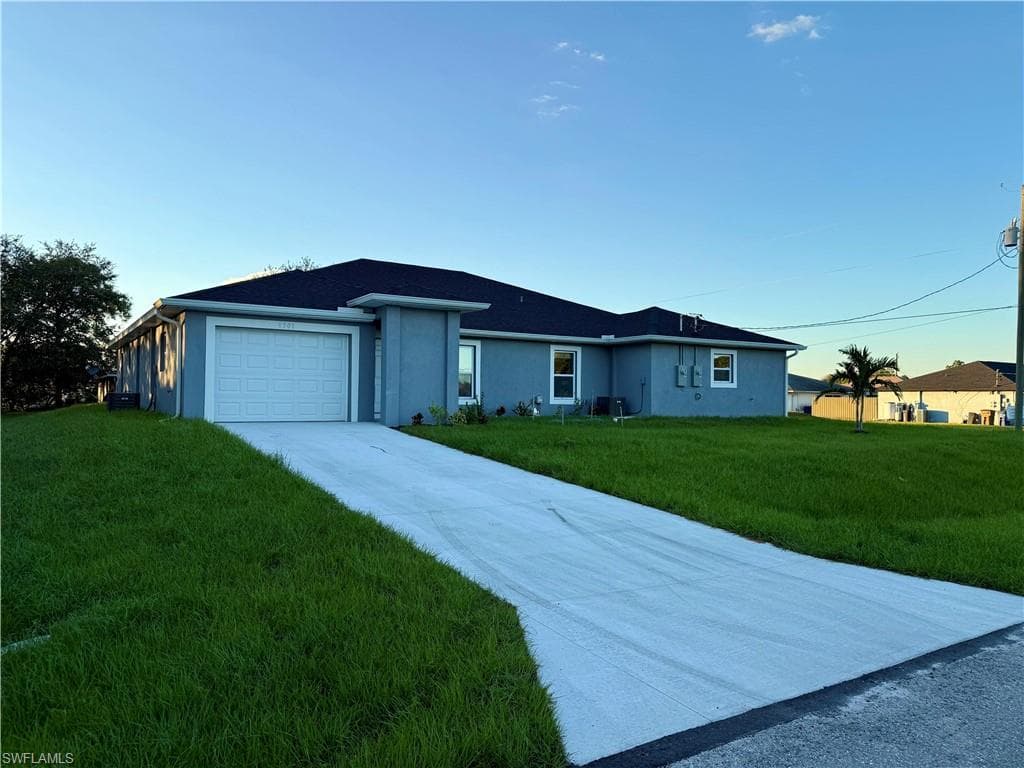 Ranch-style house featuring driveway, a front yard, stucco siding, and a garage