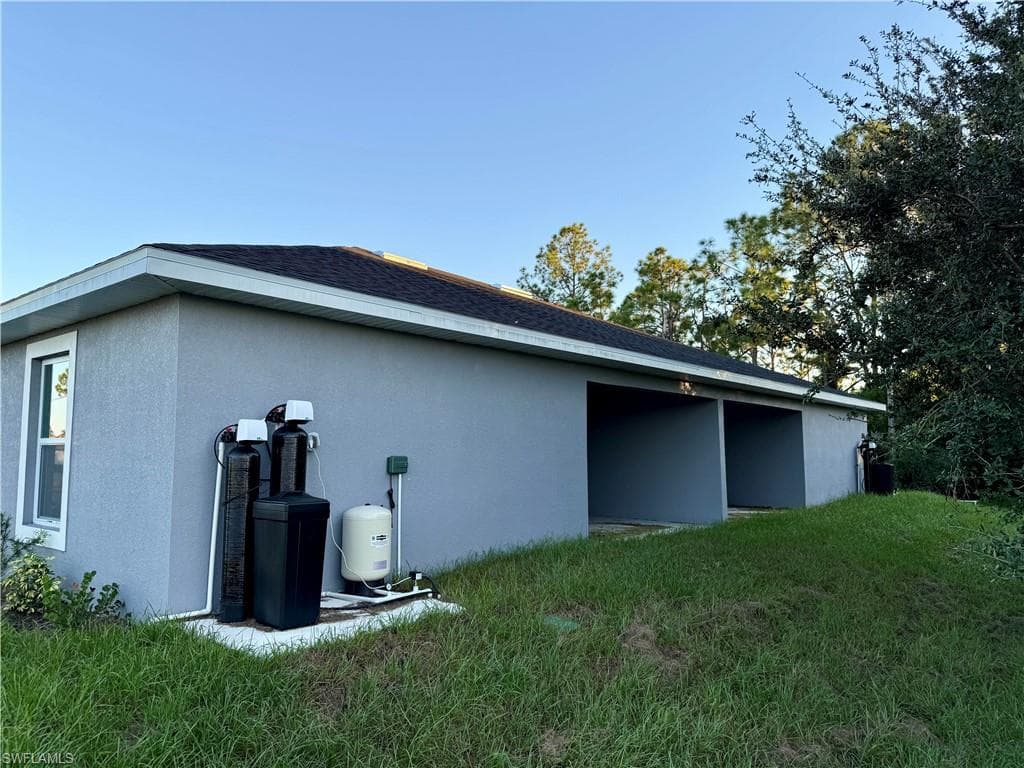 View of side of home with a lawn, stucco siding, and a shingled roof