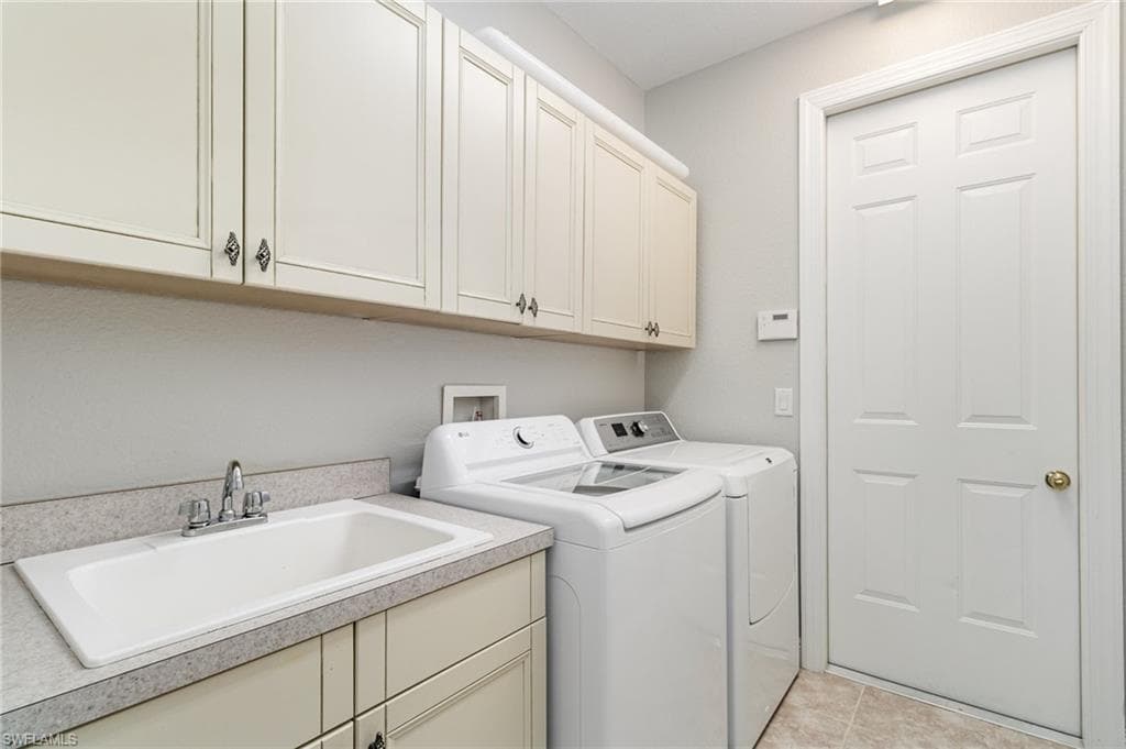 Laundry area with independent washer and dryer, light tile patterned flooring, and cabinet space