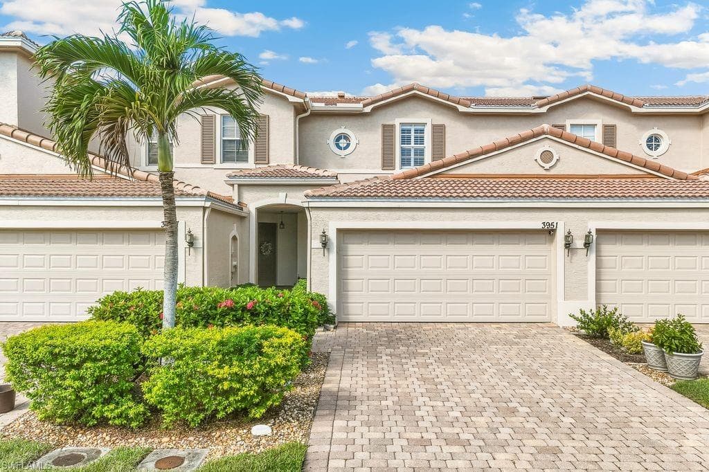 Front view of the home with a tile roof, extended decorative driveway, stucco siding, and two-car garage