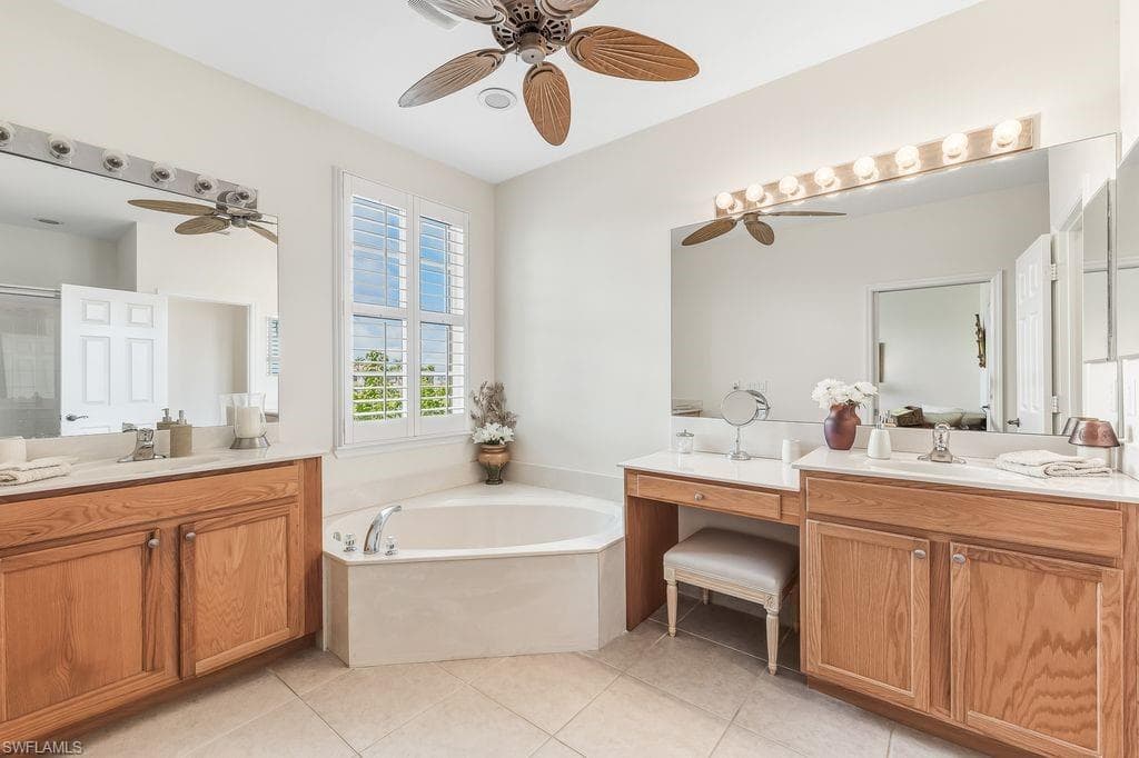 Master Bathroom with a soaking tub bath, two vanities, light tile patterned floors, walk-in shower, ceiling fan, and plantation shutters