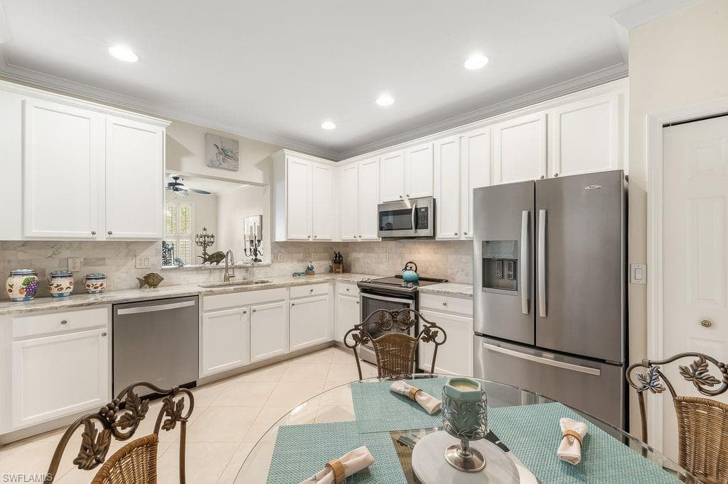 Kitchen featuring appliances with stainless steel finishes, sleek white cabinetry, light tile patterned floors, ornamental molding, and light granite counters and backsplash