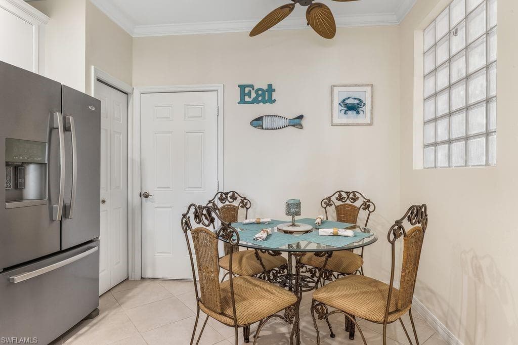 Eat-in Kitchen featuring appliances with stainless steel finishes, sleek white cabinetry, light tile patterned floors, ornamental molding, and light granite counters and backsplash