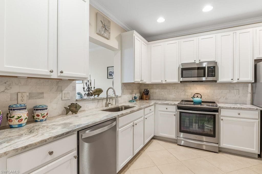 Kitchen featuring appliances with stainless steel finishes, sleek white cabinetry, light tile patterned floors, ornamental molding, and light granite counters and backsplash