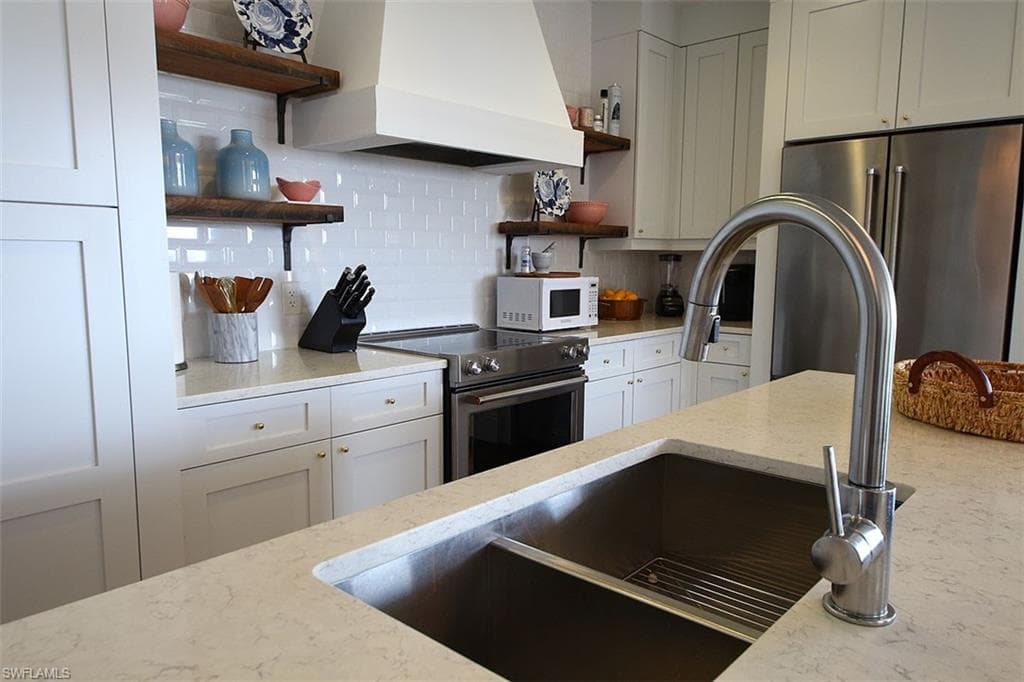 Kitchen featuring open shelves, backsplash, premium range hood, light stone counters, and stainless steel appliances