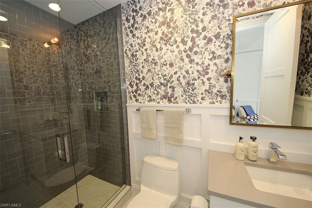 Bathroom with vanity, a stall shower, wallpapered walls, and wainscoting