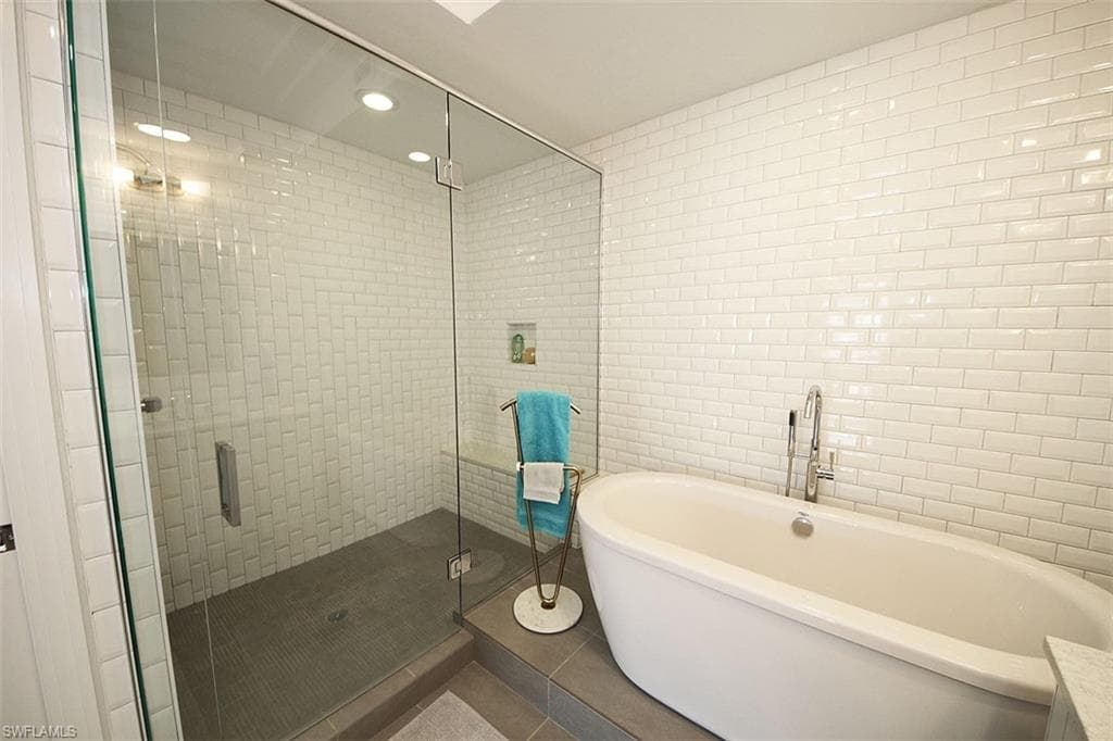 Full bath with tile walls, a stall shower, tile patterned floors, a freestanding bath, and recessed lighting