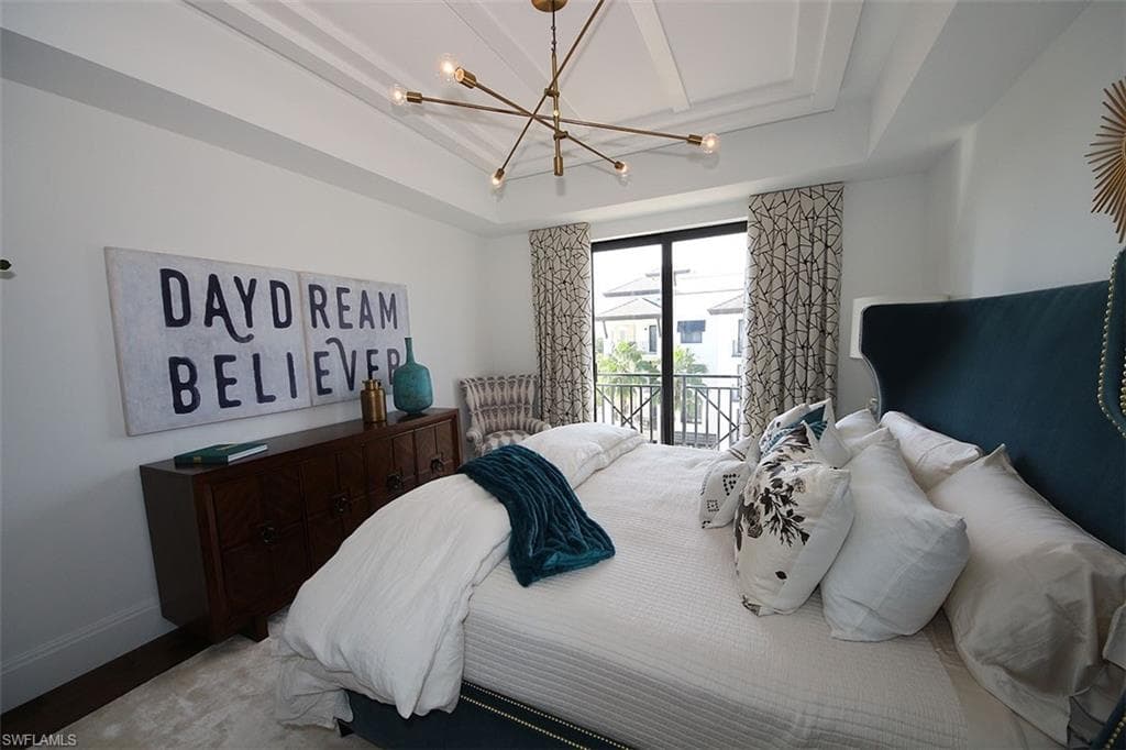 Bedroom featuring access to exterior, a tray ceiling, and a chandelier