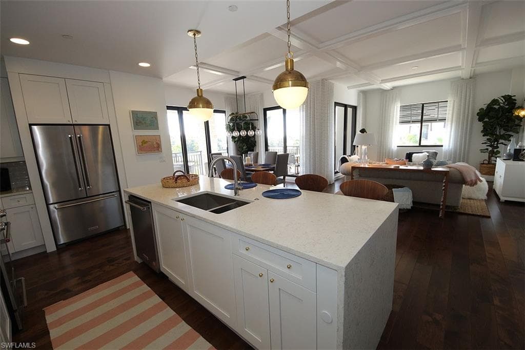 Kitchen featuring stainless steel appliances, coffered ceiling, open floor plan, white cabinets, and pendant lighting