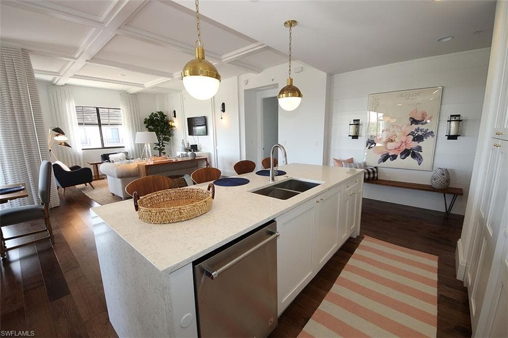 Kitchen featuring open floor plan, beam ceiling, stainless steel dishwasher, dark wood-style flooring, and light stone counters