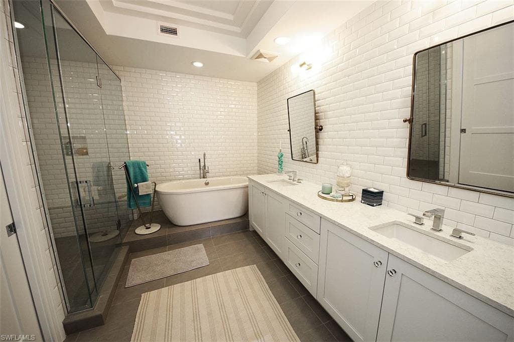 Full bathroom featuring tile walls, double vanity, dark tile patterned flooring, a soaking tub, and a stall shower