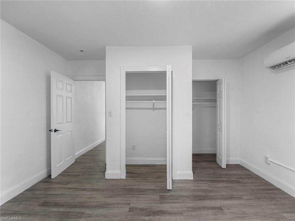Unfurnished bedroom featuring two closets, dark wood finished floors, and a wall mounted AC