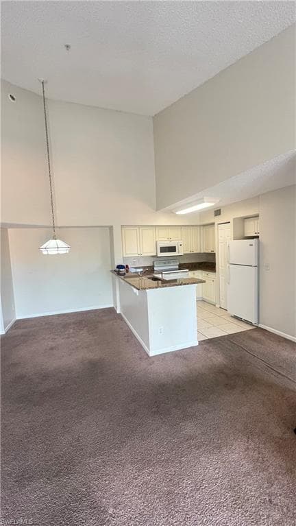Kitchen with a peninsula, white appliances, light colored carpet, high vaulted ceiling, and a textured ceiling
