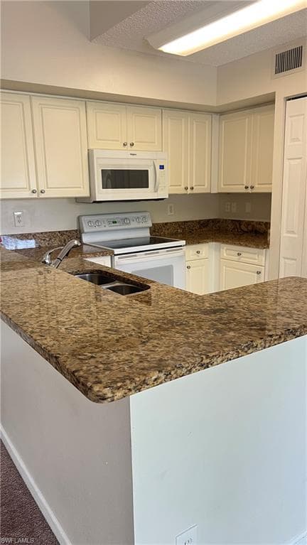 Kitchen with white appliances, dark stone counters, white cabinets, a peninsula, and a textured ceiling