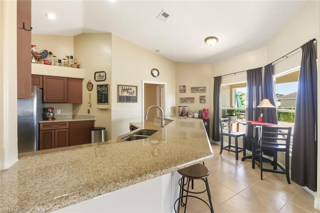 Kitchen featuring freestanding refrigerator, light stone counters, light tile patterned flooring, a breakfast bar, and brown cabinets