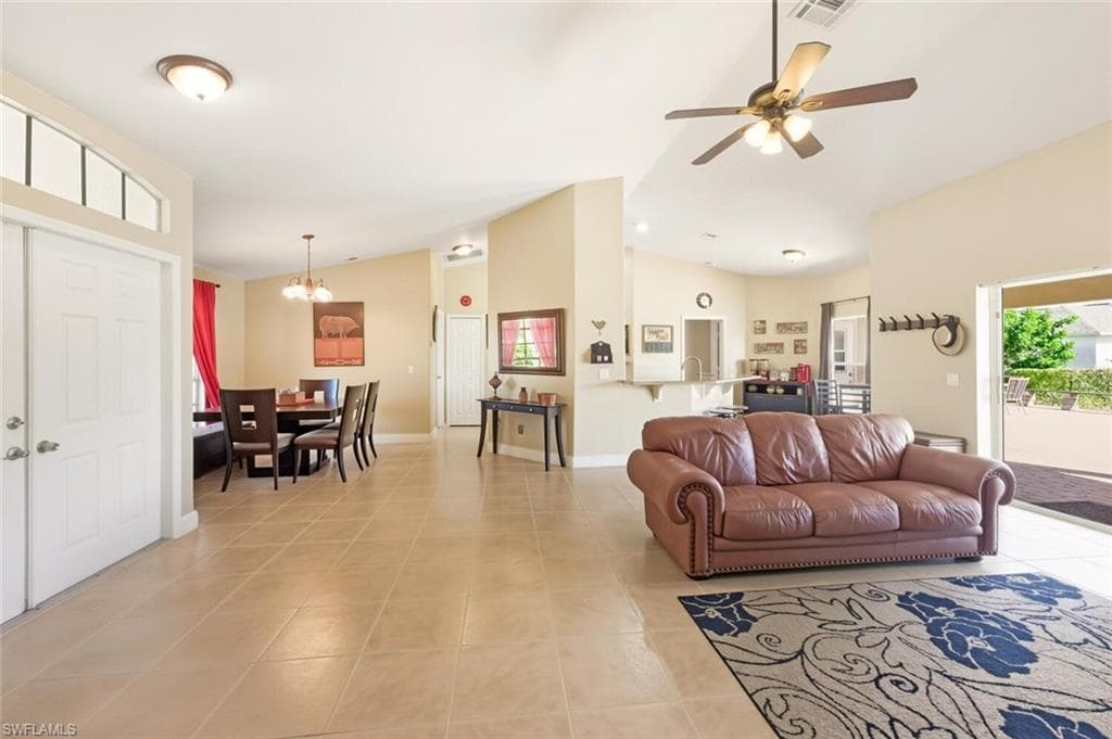 Living room featuring healthy amount of natural light, lofted ceiling, light tile patterned floors, a chandelier, and ceiling fan