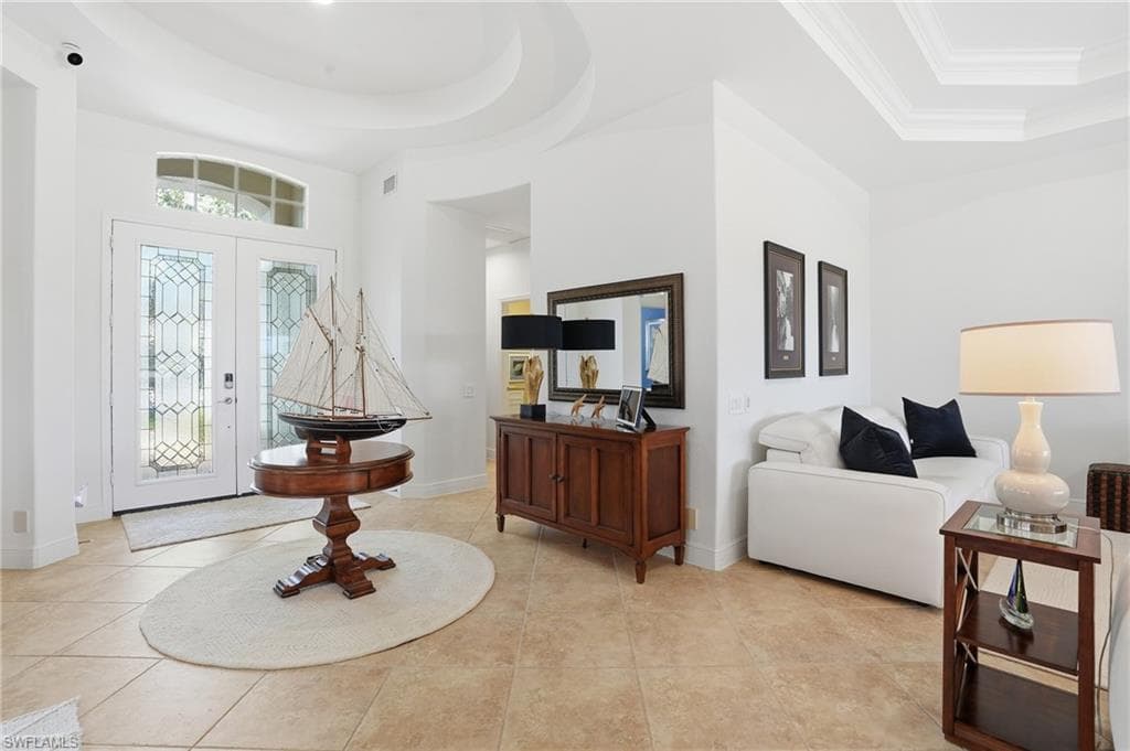 Entrance foyer featuring a tray ceiling, light tile patterned flooring, crown molding, and french doors