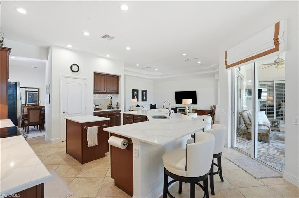 Kitchen with light stone countertops, a breakfast bar, recessed lighting, light tile patterned floors, and freestanding refrigerator