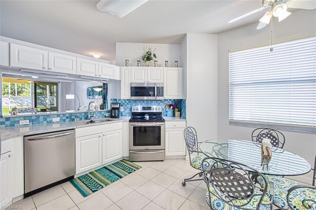Kitchen featuring stainless steel appliances, tasteful backsplash, white cabinets, light stone countertops, and light tile patterned floors