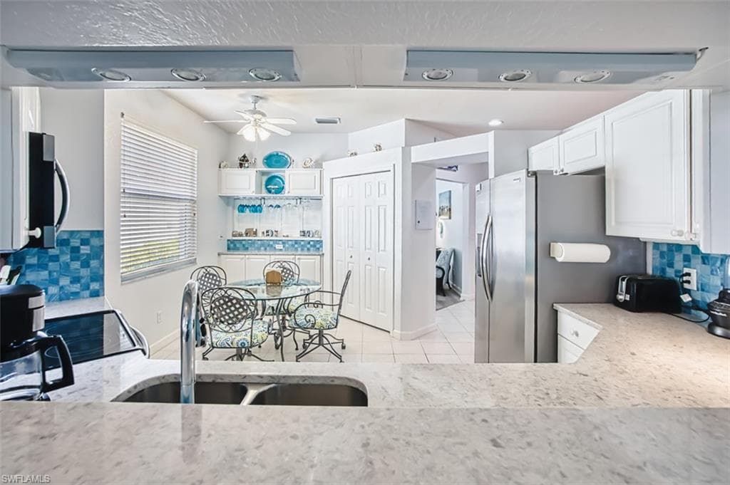 Kitchen with decorative backsplash, white cabinetry, stainless steel appliances, light stone countertops, and a ceiling fan