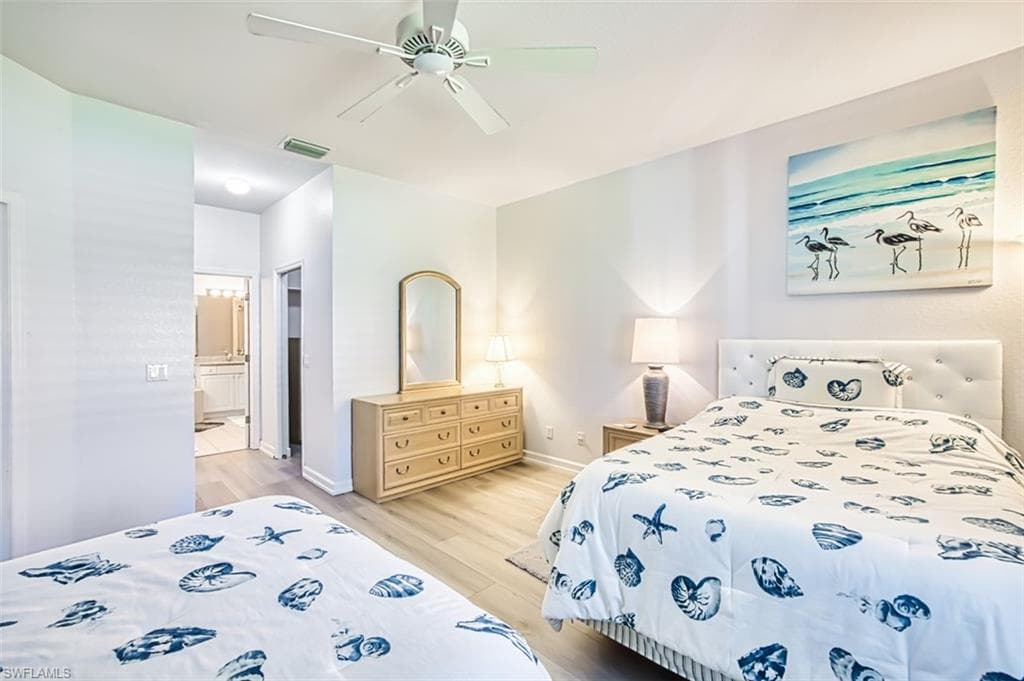 Bedroom featuring light wood-style floors, ceiling fan, and ensuite bath