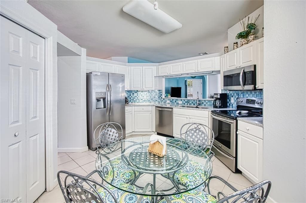 Kitchen featuring appliances with stainless steel finishes, white cabinetry, decorative backsplash, and light tile patterned floors